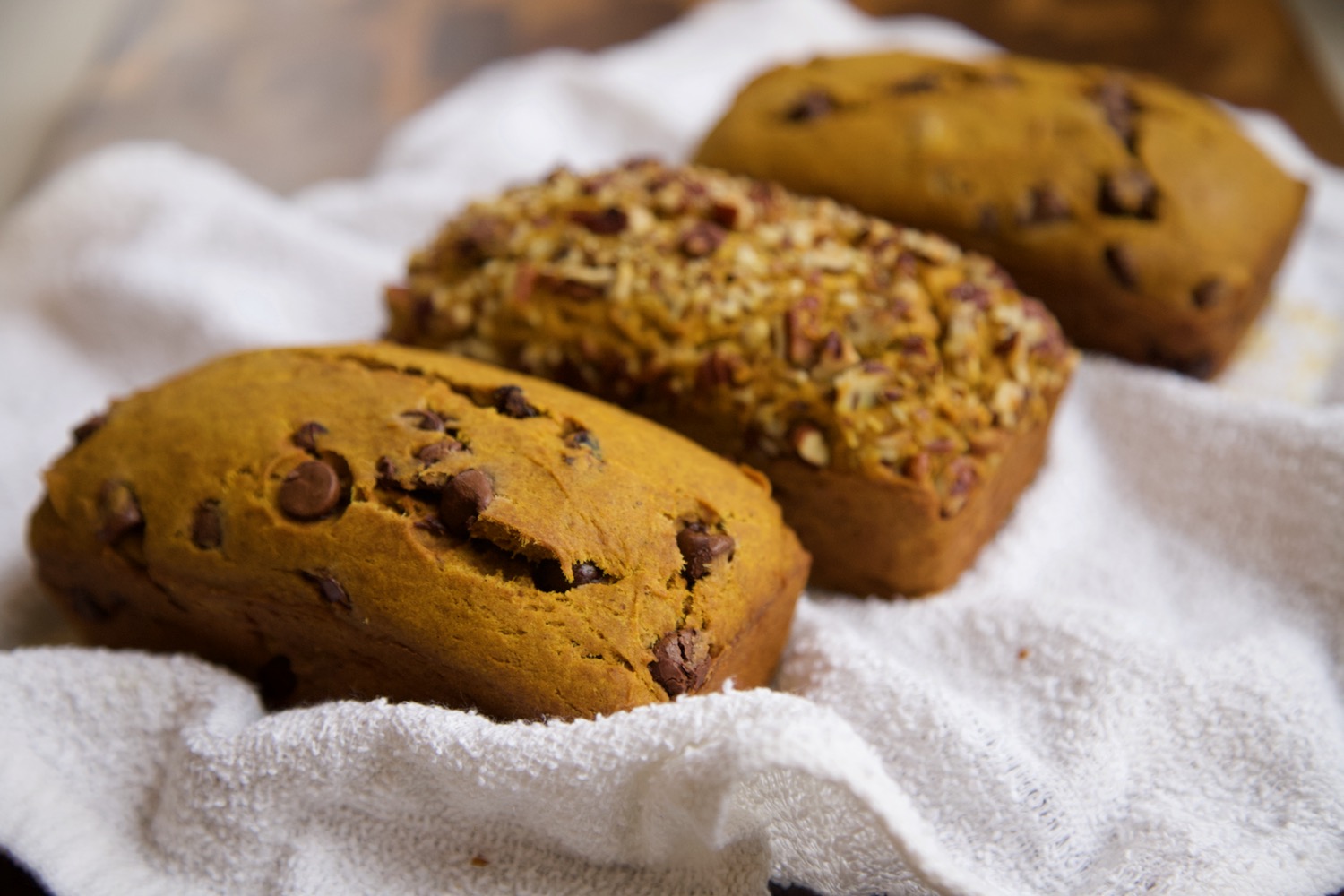 Three loaves of pumpkin bread sitting on a hand kitchen towel.