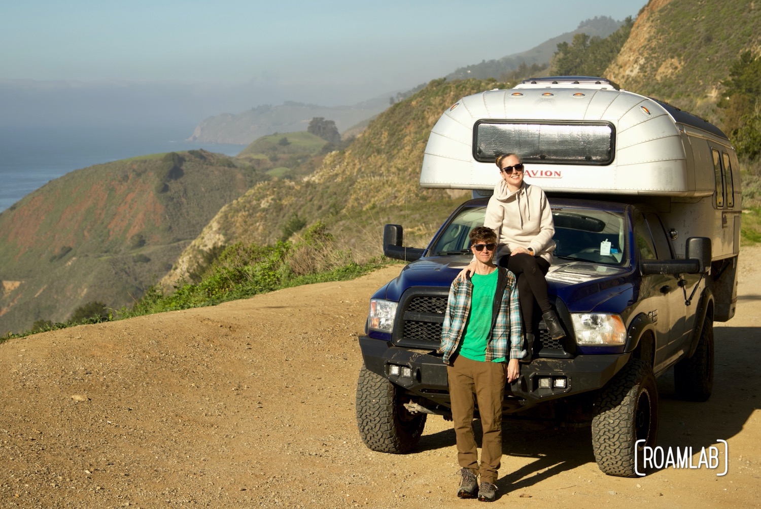 Lexi and Chris from Roam Lab, sitting on their 1970 Avion C11 truck camper on a pulloff off Highway 1 in Big Sur, California.