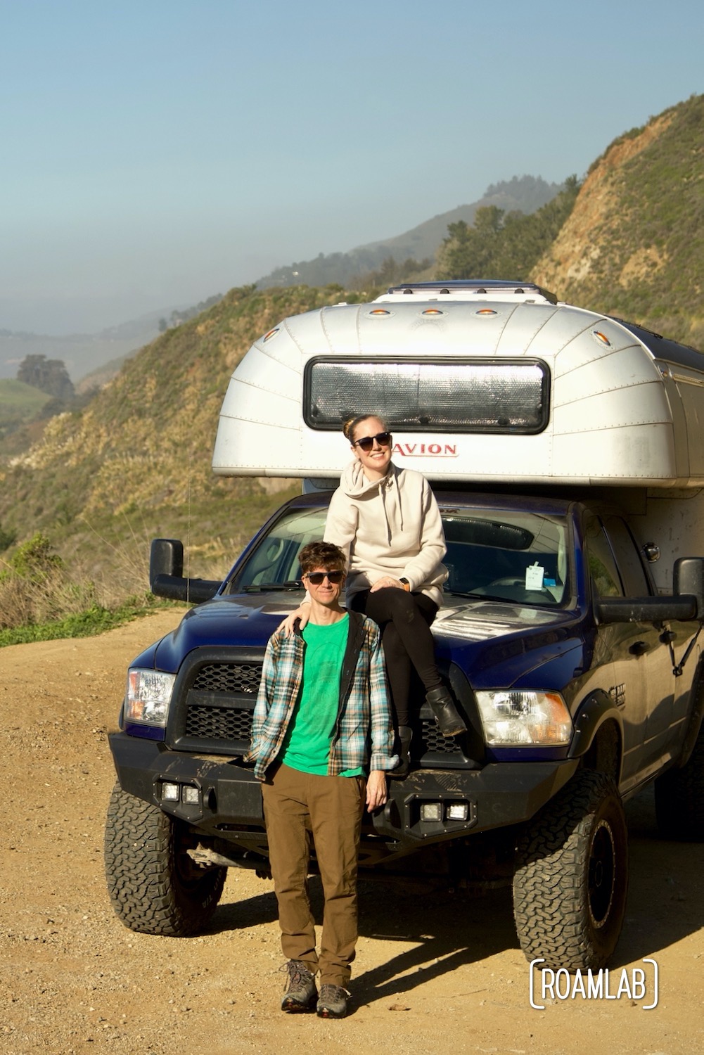 Lexi and Chris from Roam Lab, sitting on their 1970 Avion C11 truck camper on a pulloff off Highway 1 in Big Sur, California.