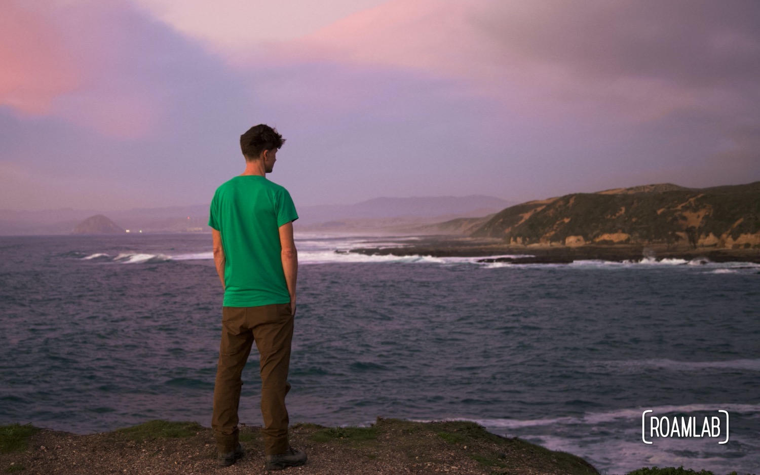 Man in a green shirt walking the coastline of Montaña de Oro State Park at sunset.