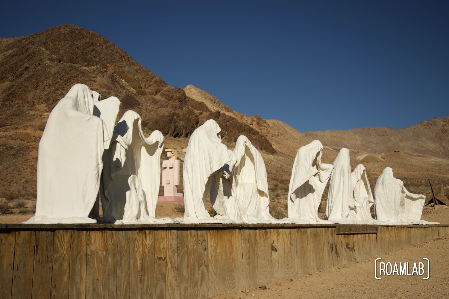 Plaster ghost sculptures in the form of the last supper on a wood platform.