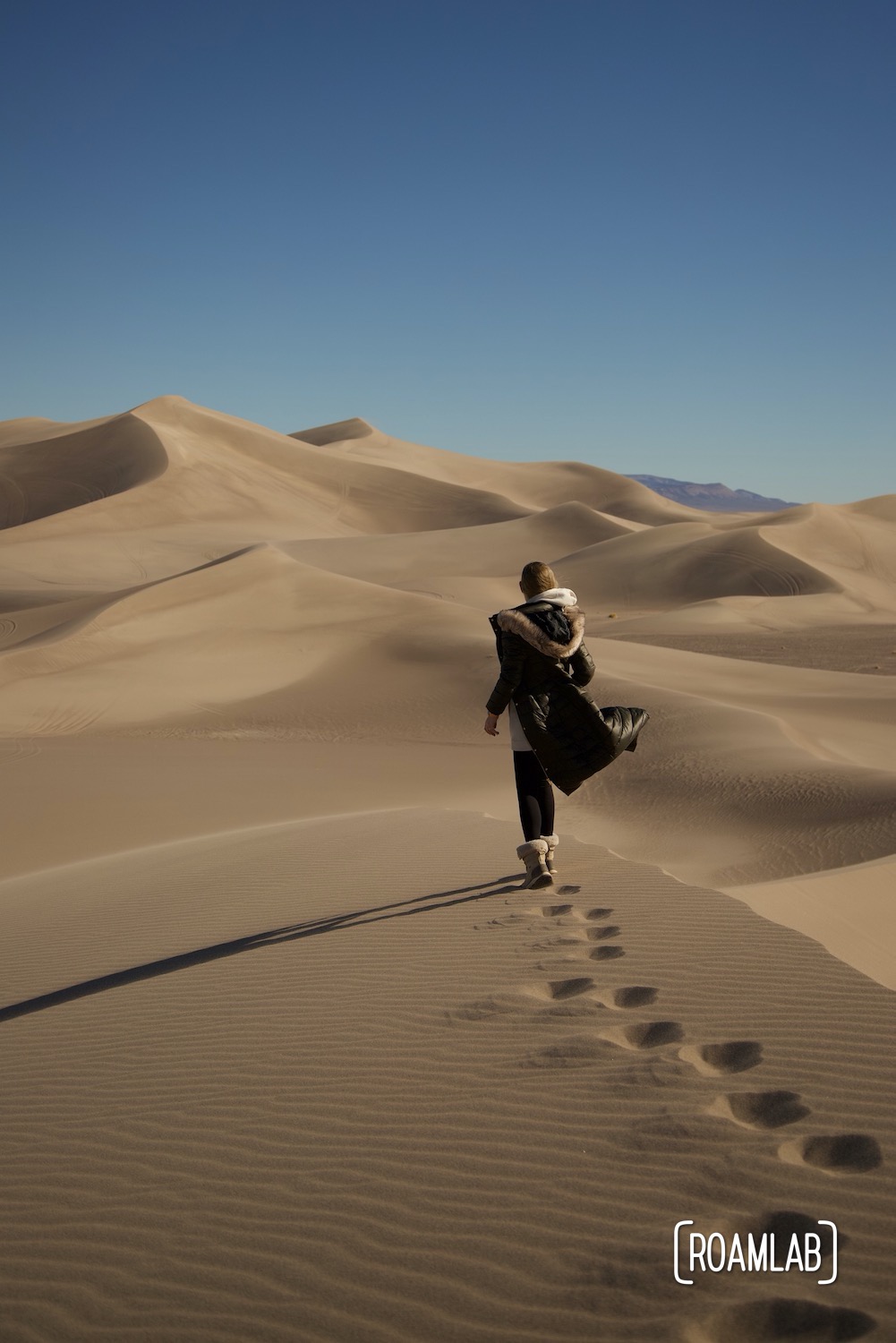 Woman walking away and leaving footprints in the sandy ridge of Big Dune Recreational Area in Nevada.