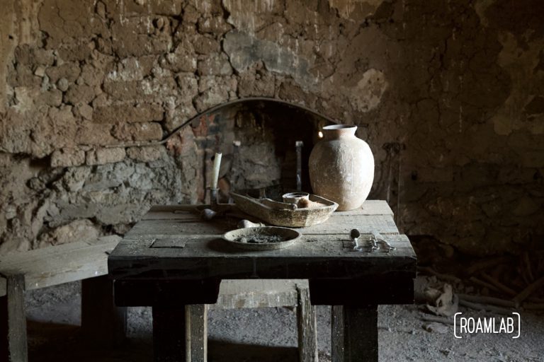 Pitcher, dishes, and cutlery on an old wooden table in an aging brick building in Shakespeare Ghost Town, New Mexico.