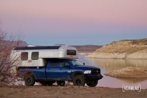 1970 Avion C11 truck camper parked along the shore of Elephant Butte Lake at sunset.