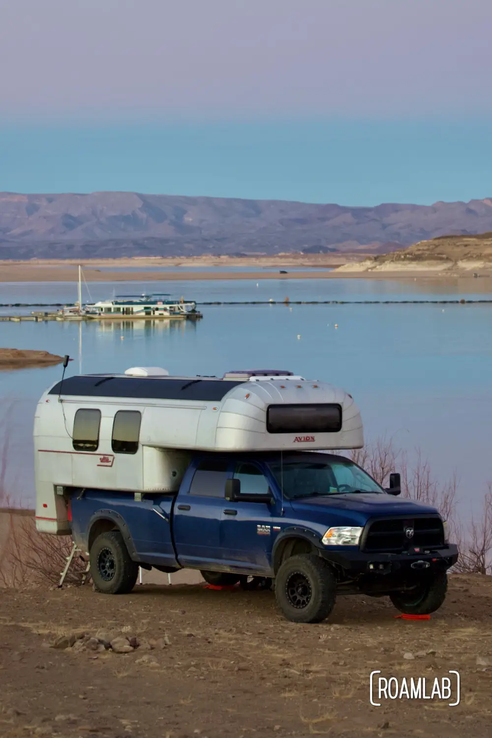 1970 Avion C11 truck camper parked on the shore of Elephant Butte Lake at dusk.