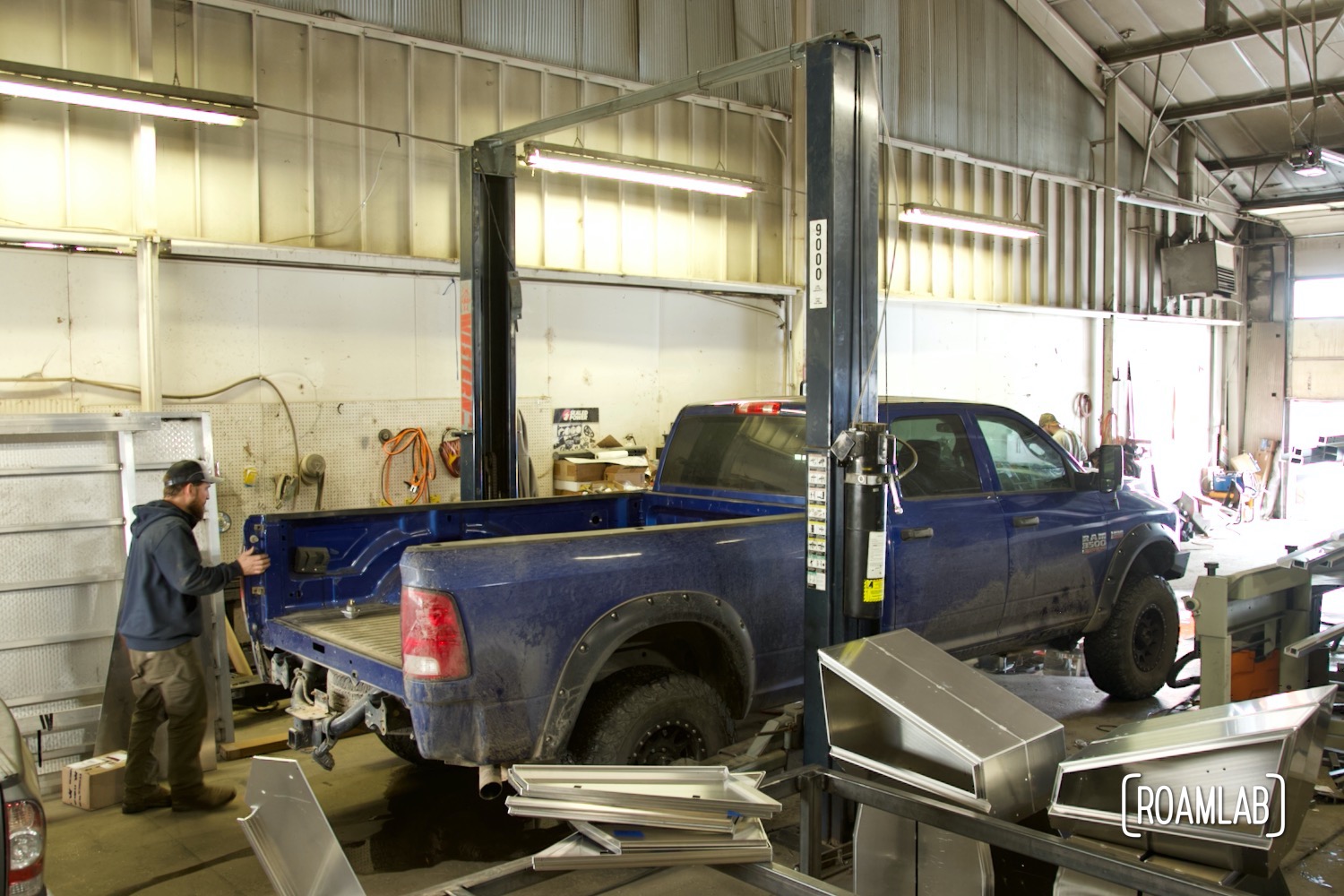 Man walking around blue truck parked in an industrial garage.