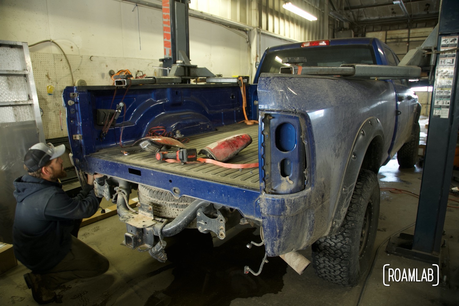 Man reaching under a blue truck bed, disconnecting brake lights.