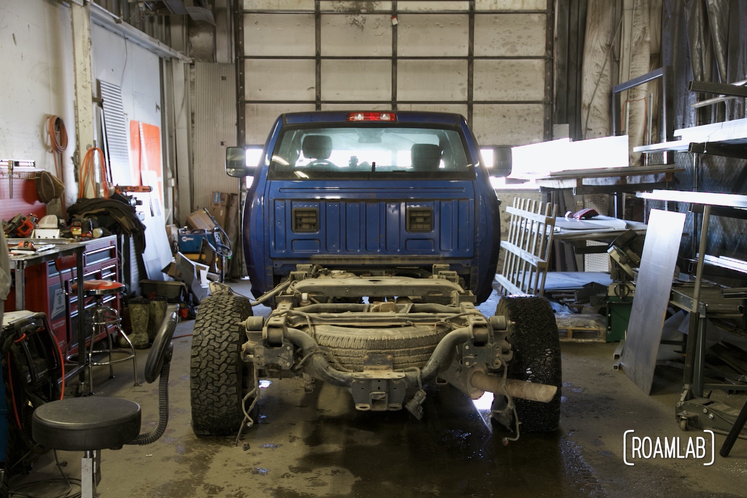 Blue truck parked in an industrial garage with truck bed removed, exposing the frame.