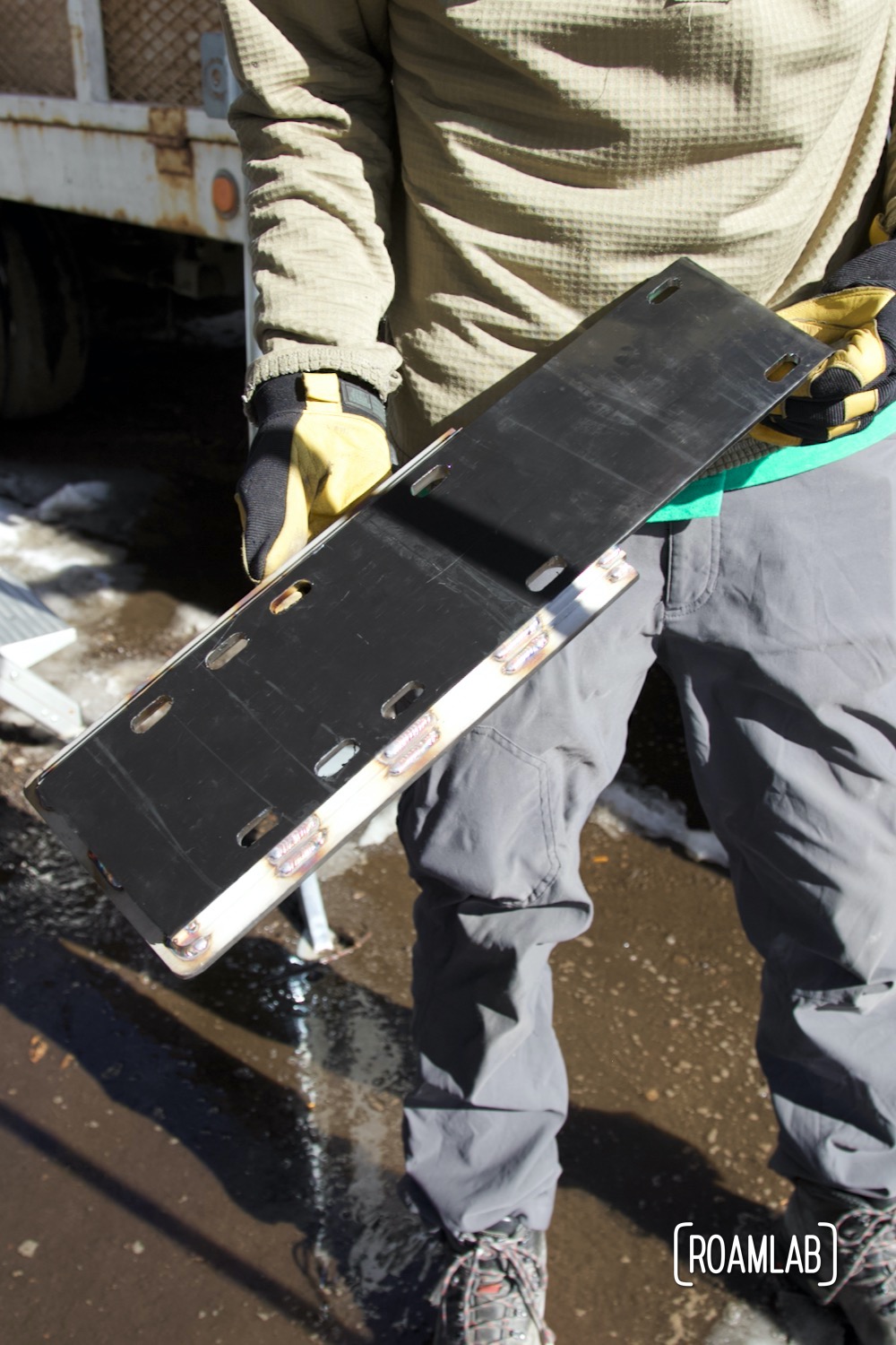 Man holding a custom stainless steel jack point before installing it on a truck camper.