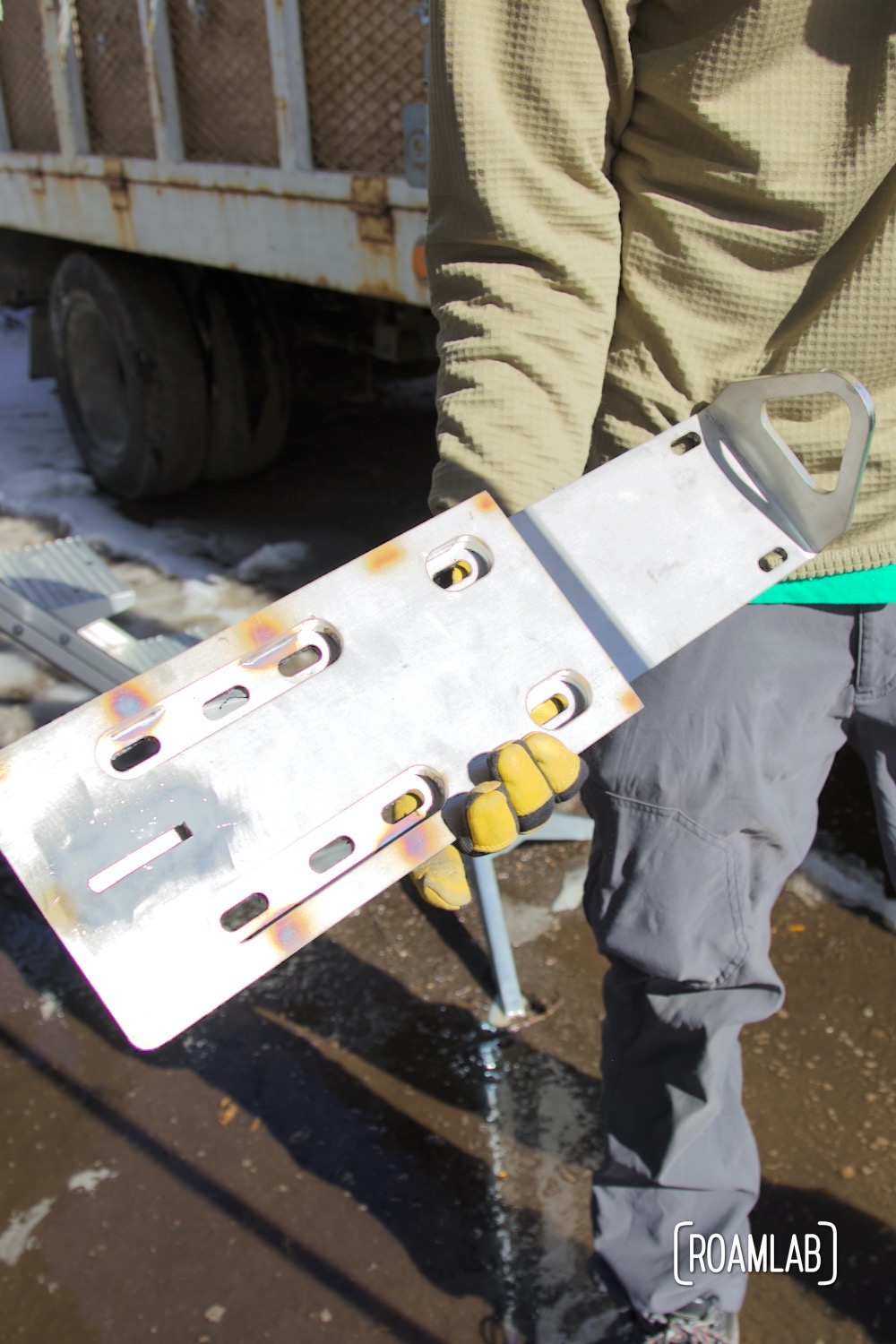 Man holding a custom stainless steel jack point before installing it on a truck camper.