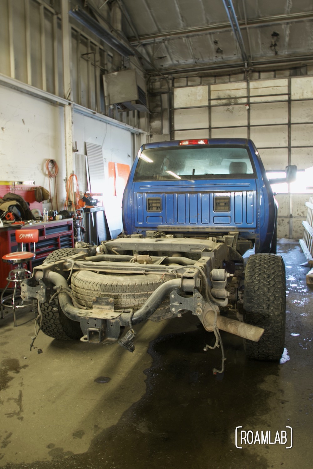 Blue truck parked in a garage without a truck bed, exposing inner workings of the frame.