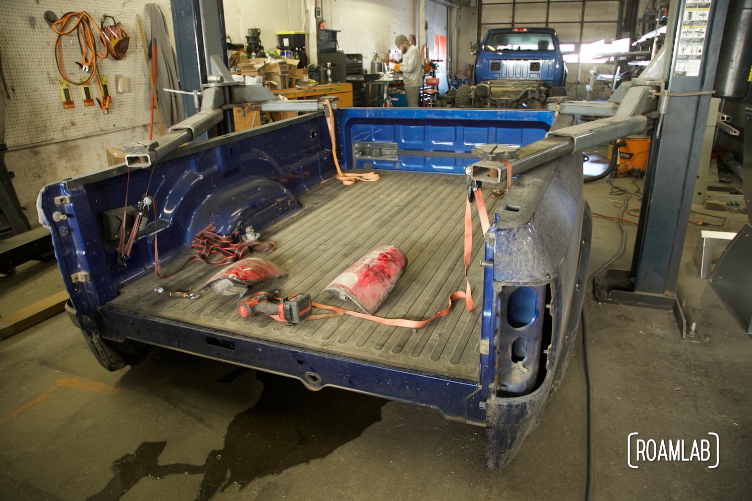 Blue Ram 3500 truck bed suspended on a lift with truck cab parked in the background.