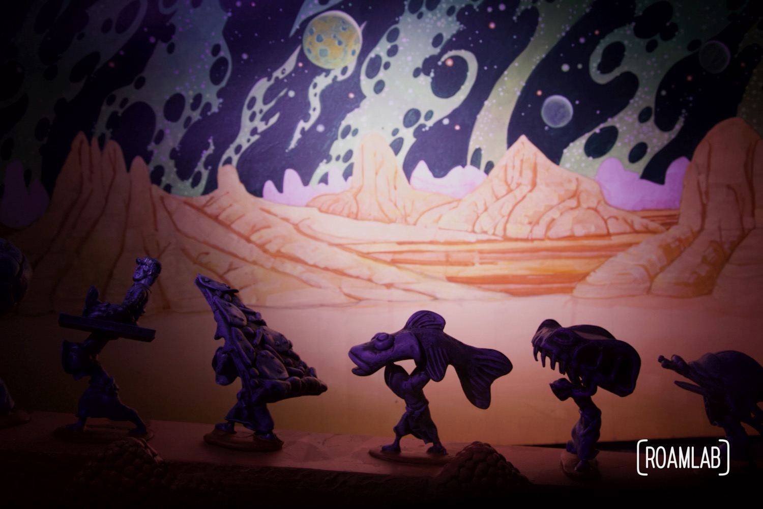 Diorama of strange creatures carrying pizza, fish, and other oddities along an alien landscape.