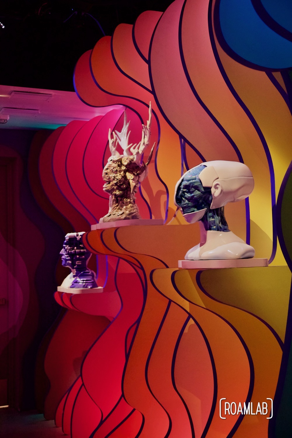 Three humanoid busts mounted on a rippling wall in Meow Wolf's Denver, Colorado location, Convergence Station.