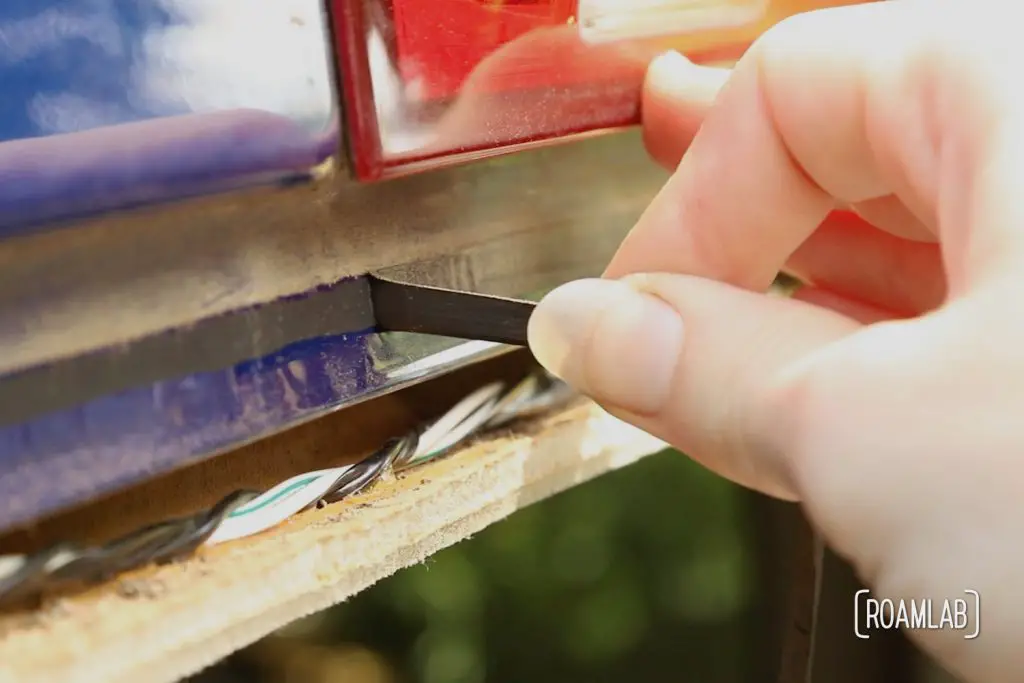 Hand pulling a thin black strip of urethane away from a blue metal frame of a truck cab.