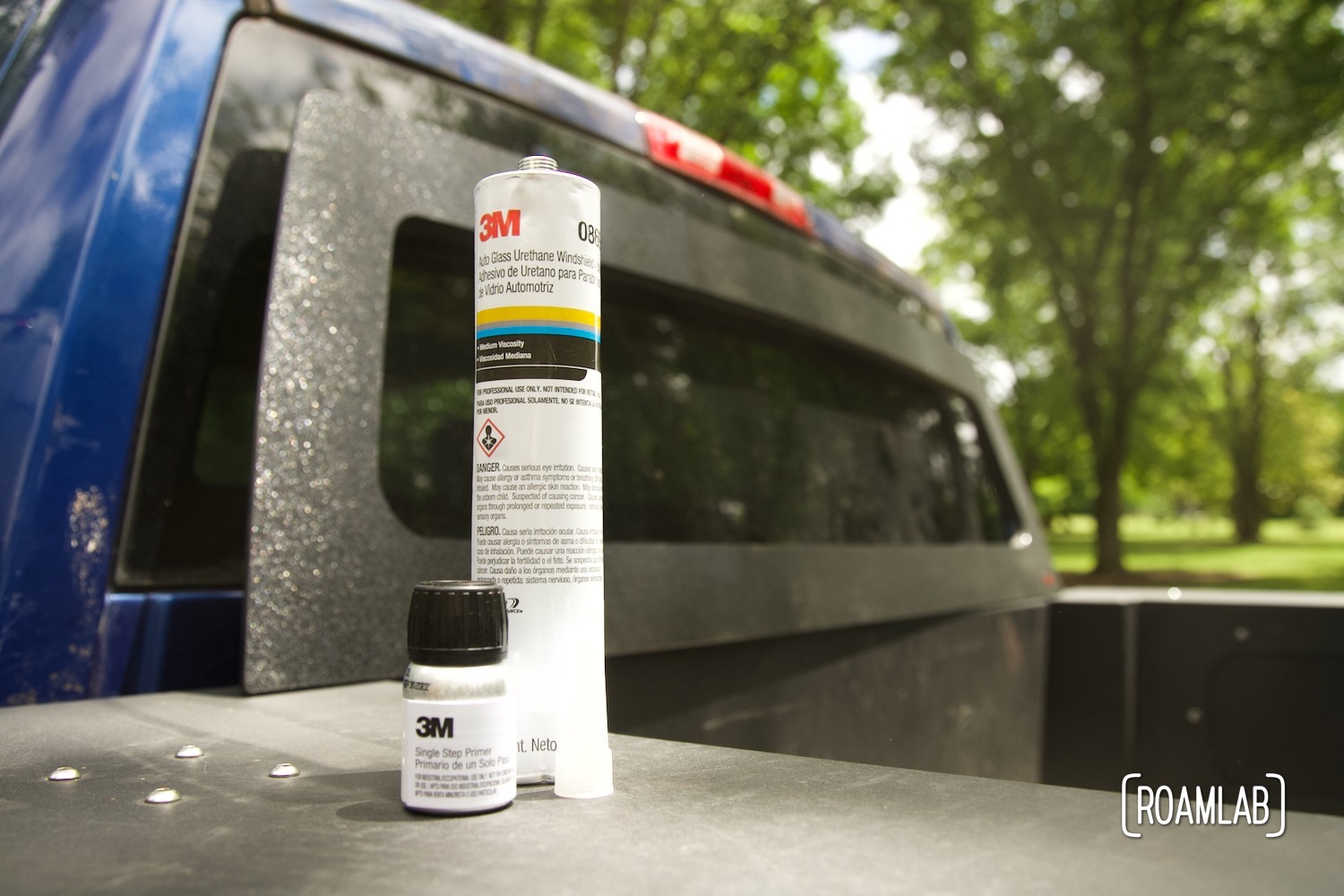 Bottle of primer and tube of urethane sitting on a truck bed box in front of a rear cab window.