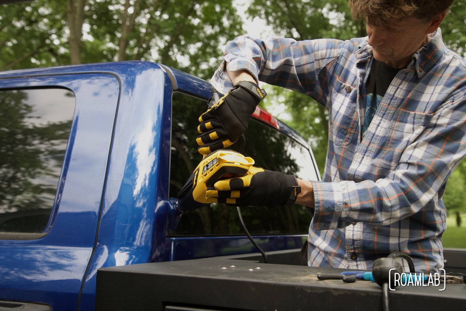 Man holding a heat gun up to the edge of a windshield pane.