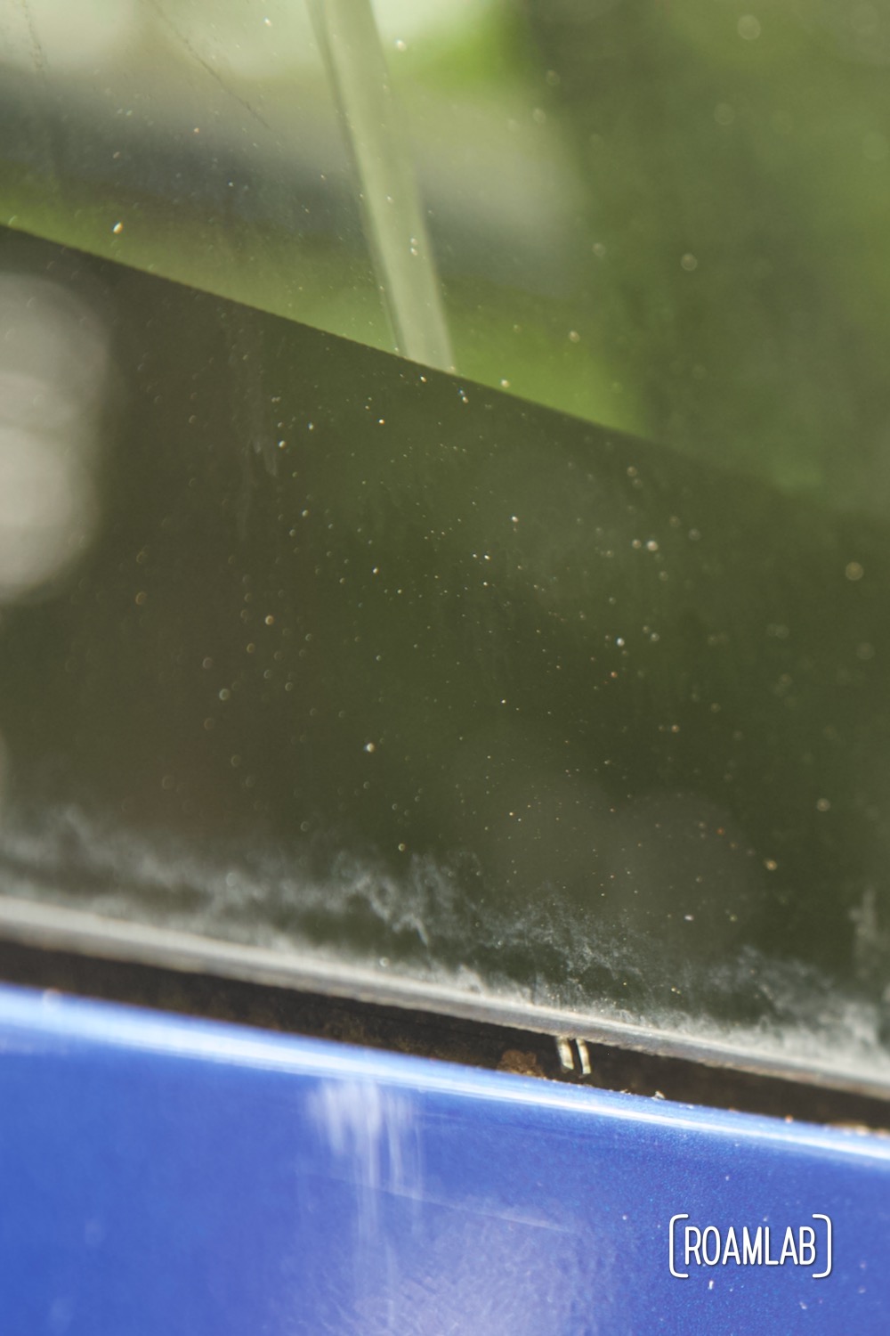 Tip of wire feeder peaking through narrow gap between the truck's black windshield glass and blue metal frame.