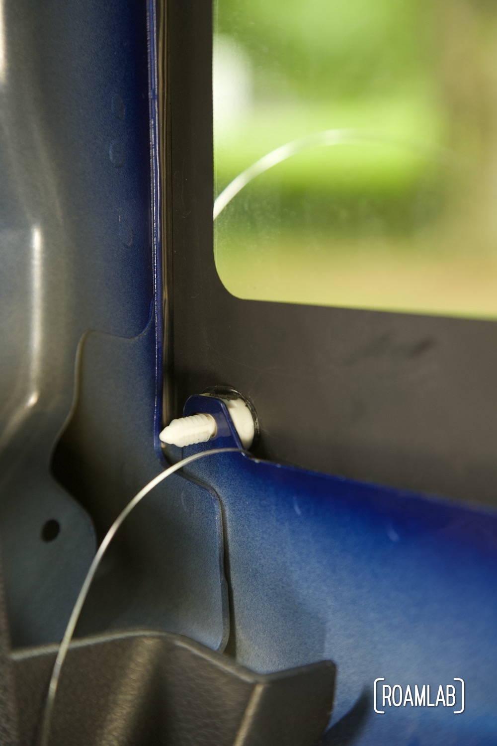 Cutting wire emerging from a gap between black windshield glass and blue metal frame with a plastic spacer obstructing further progress.