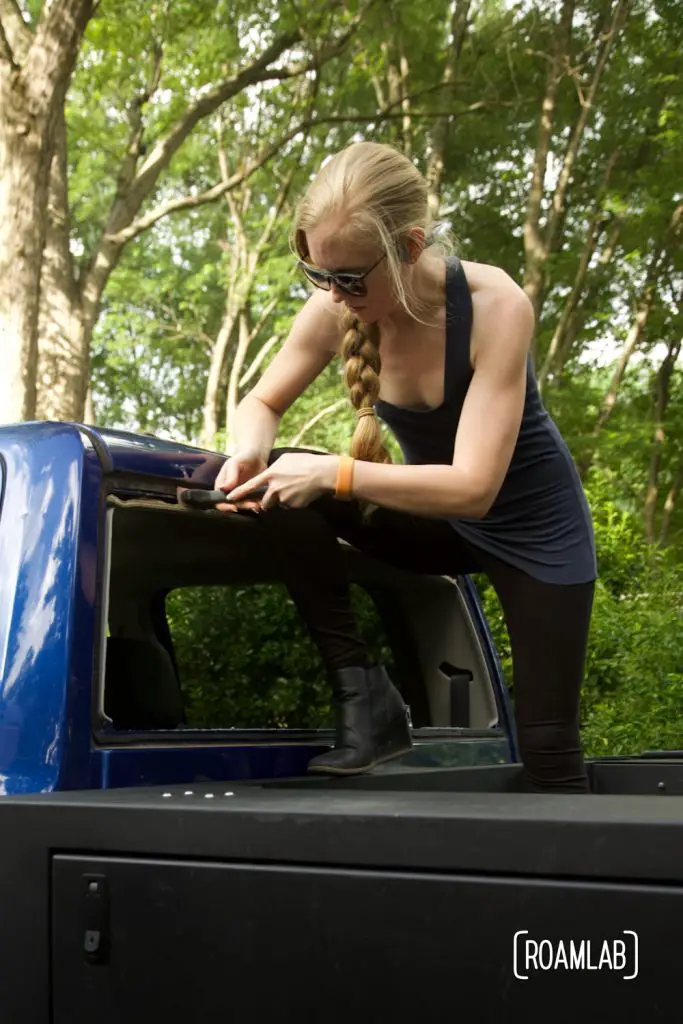 Woman trimming away excess urethane from the truck's rear windshield frame.