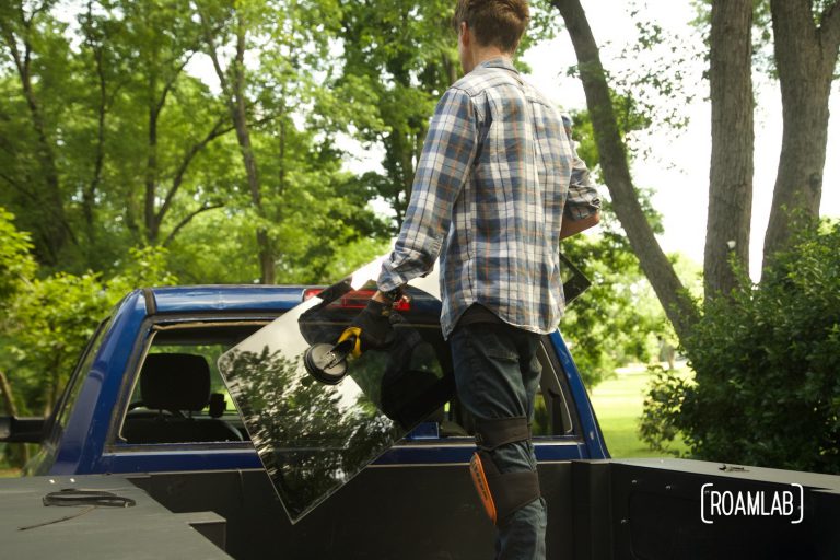 Man using suction cup handles to pull away a loose rear windshield window from the truck cab.
