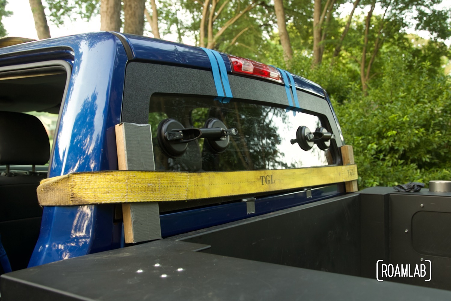 Read truck window secured in place with blue masking tape and a yellow ratcheting strap.