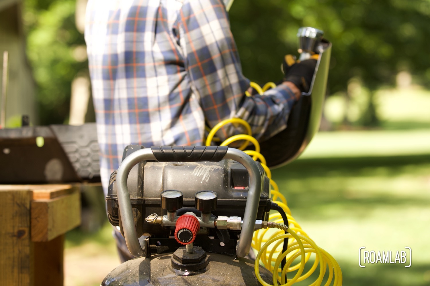 Air compressor in the foreground with a yellow cord connected to a cut-off tool held by a man in the background.