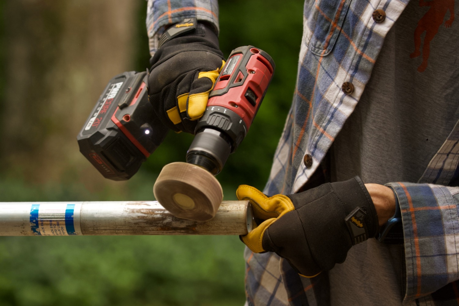 Gloved hands holding a power drill with an abrasive flapper wheel attachment to grind off corrosion on a steel jack.