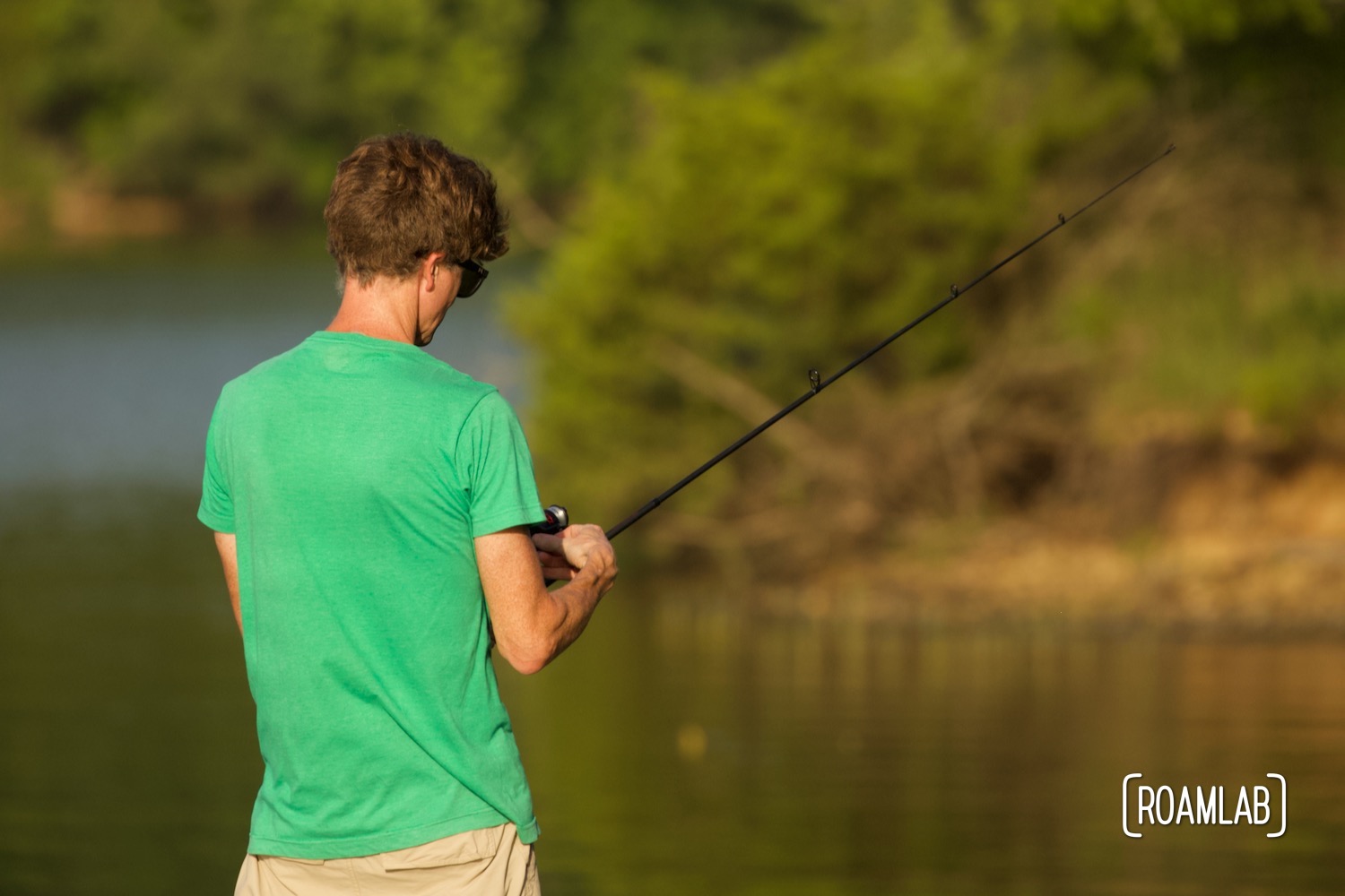 Man standing along the lakeside holding a fishing rod.