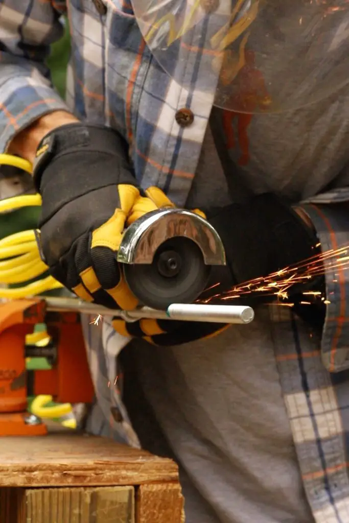 Threaded metal rod secured in an orange worktable vice as a man sends sparks flying with a cut-off tool.