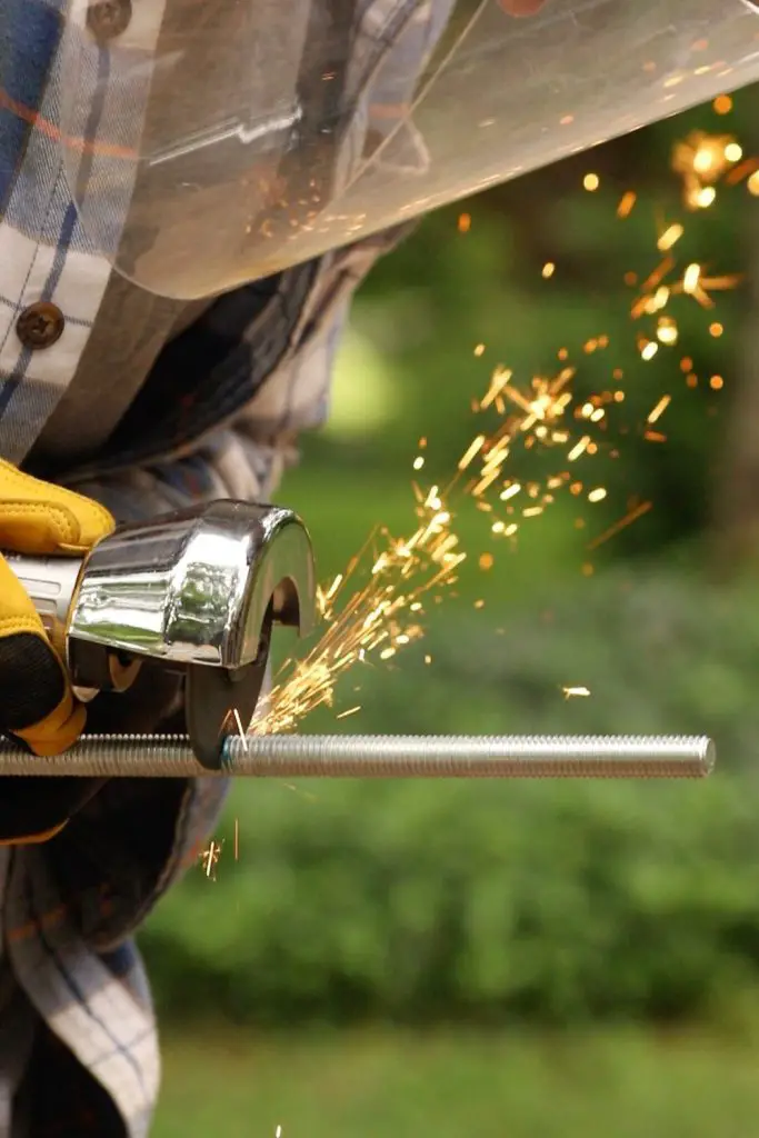Gloved hand holding a cutoff tool to a threaded metal rod as sparks fly.