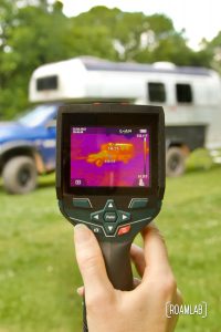 Hand holding a thermal camera revealing hot spots on a vintage Avion C11 truck camper.