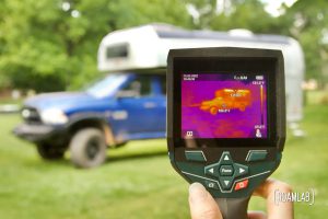 Hand holding a thermal camera revealing hot spots on a vintage Avion C11 truck camper.