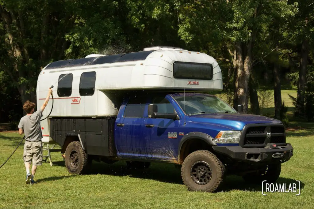 Man using a hose to spray water on solar panels mounted to the roof of an Avion C11 truck camper.