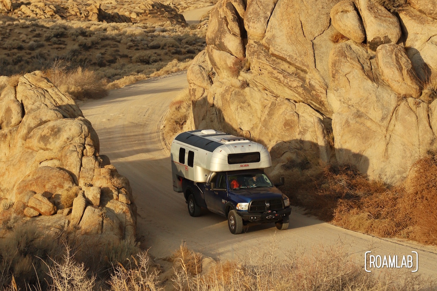 Avion C11 truck camper driving on a dirt road, dwarfed by golden boulders of the Alabama Hills in the Eastern Sierras in southern California.