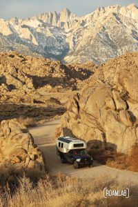 Avion C11 truck camper driving on a dirt road, dwarfed by golden boulders of the Alabama Hills in the Eastern Sierras in southern California.