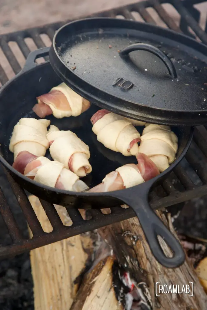 Prosecute and cheese mini croissants baking over a campfire in a cast iron skillet.