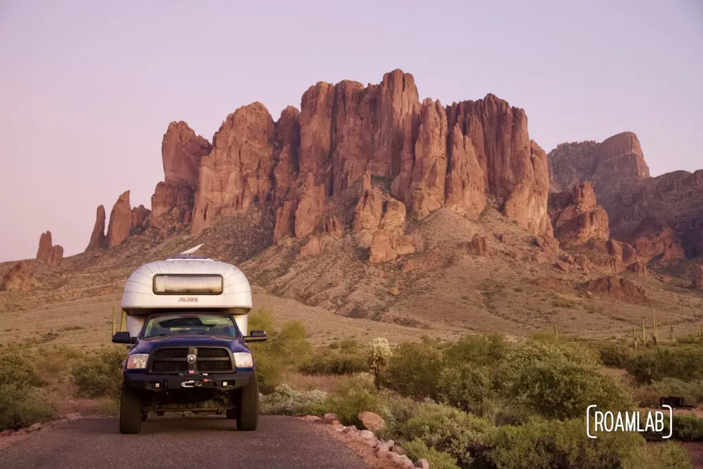 1970 Avion C11 truck camper parked in front of the Superstition Mountains in Lost Dutchman State Park at sunset.