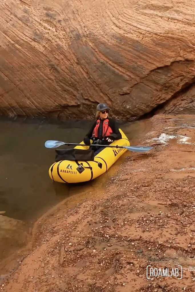 Woman in a yellow raft along the pink sandy shore of Antelope Canyon.