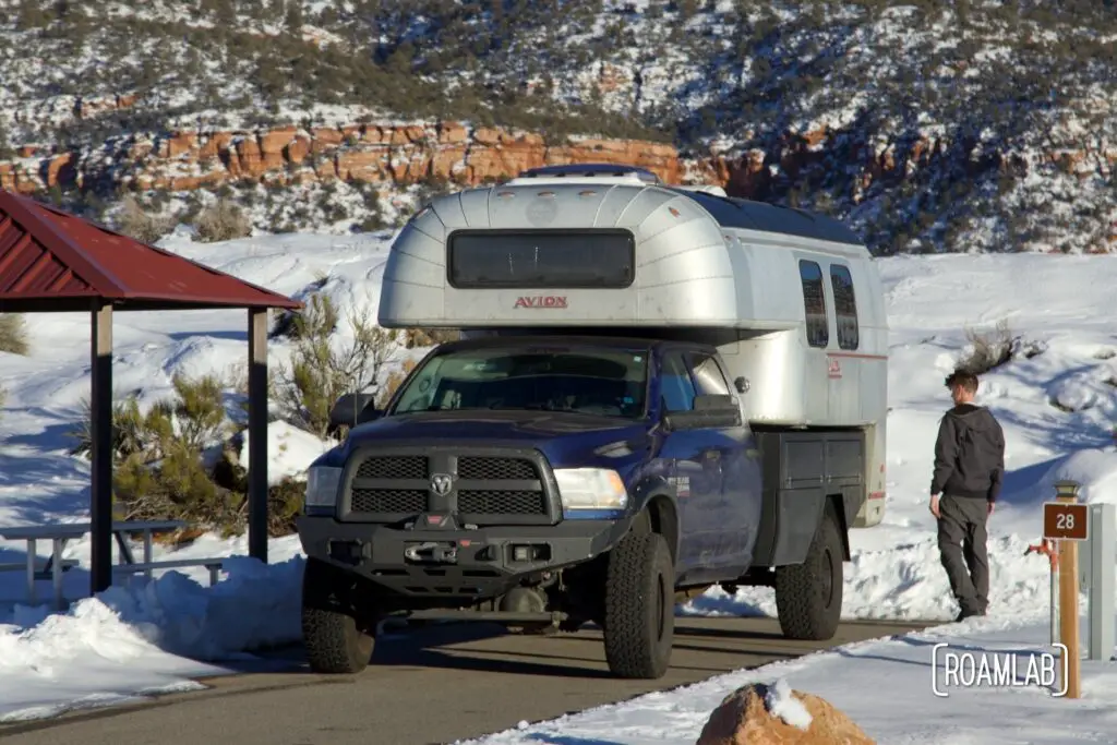 Avion C11 truck camper parked on a shoveled paved campsite surrounded by snow drifts.