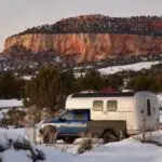 Avion C11 truck camper parked among snow drifts at sunset with pink cliffs rising in the distance at Coral Pink Sand Dunes State Park in Northern Arizona.
