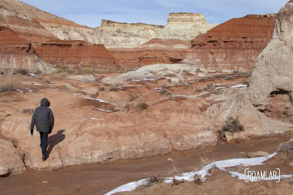 Man hiking up a red sandstone wash with snow.