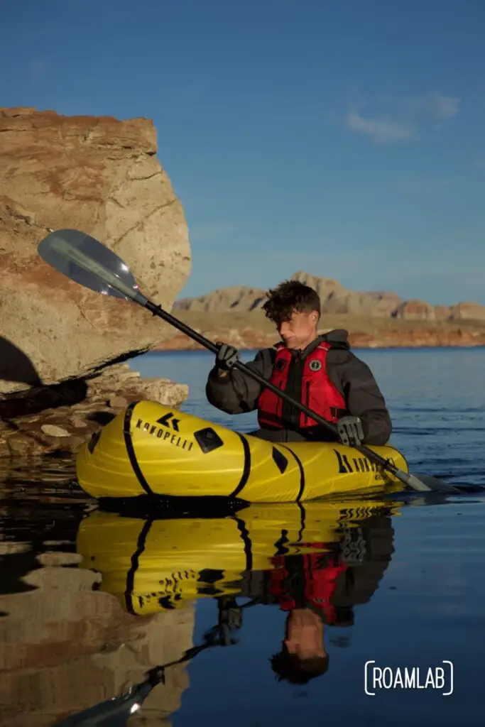 Man in a yellow raft paddling past a yellow rock in Lake Powell.