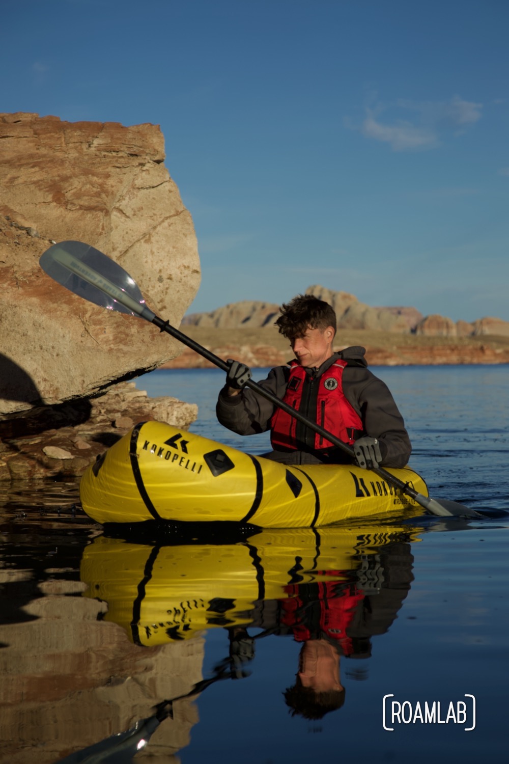 Man in a yellow raft paddling past a yellow rock in Lake Powell.