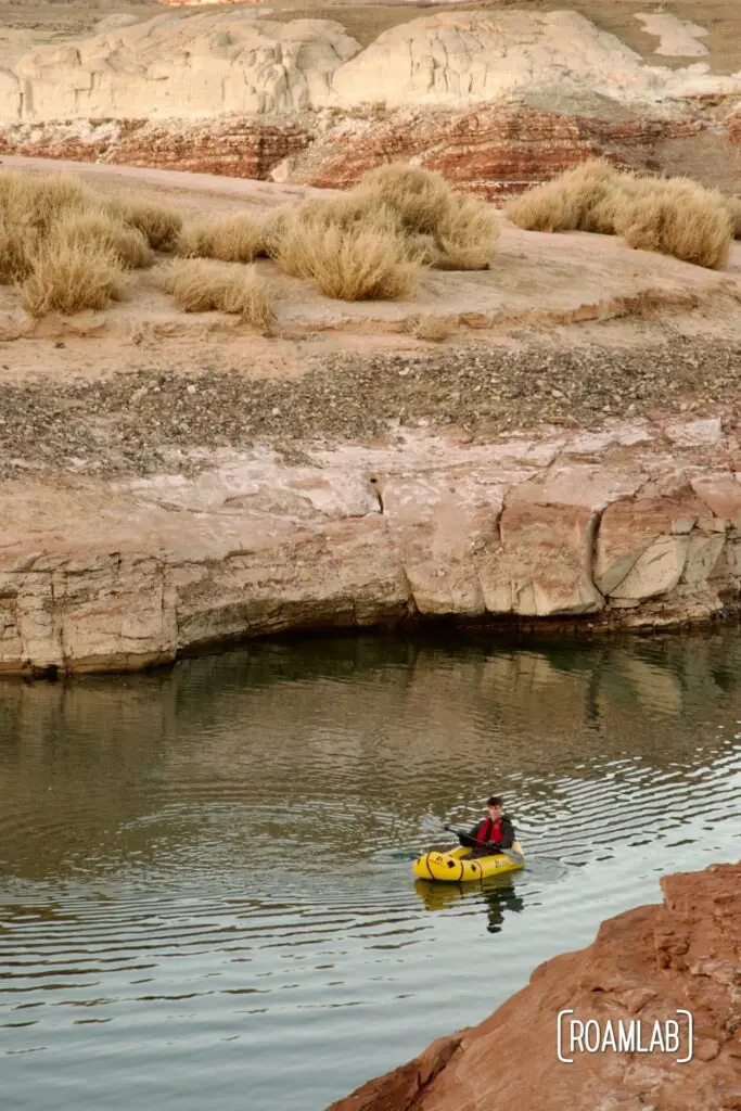Man in a yellow raft paddling along the pink buttes of Lake Powell.
