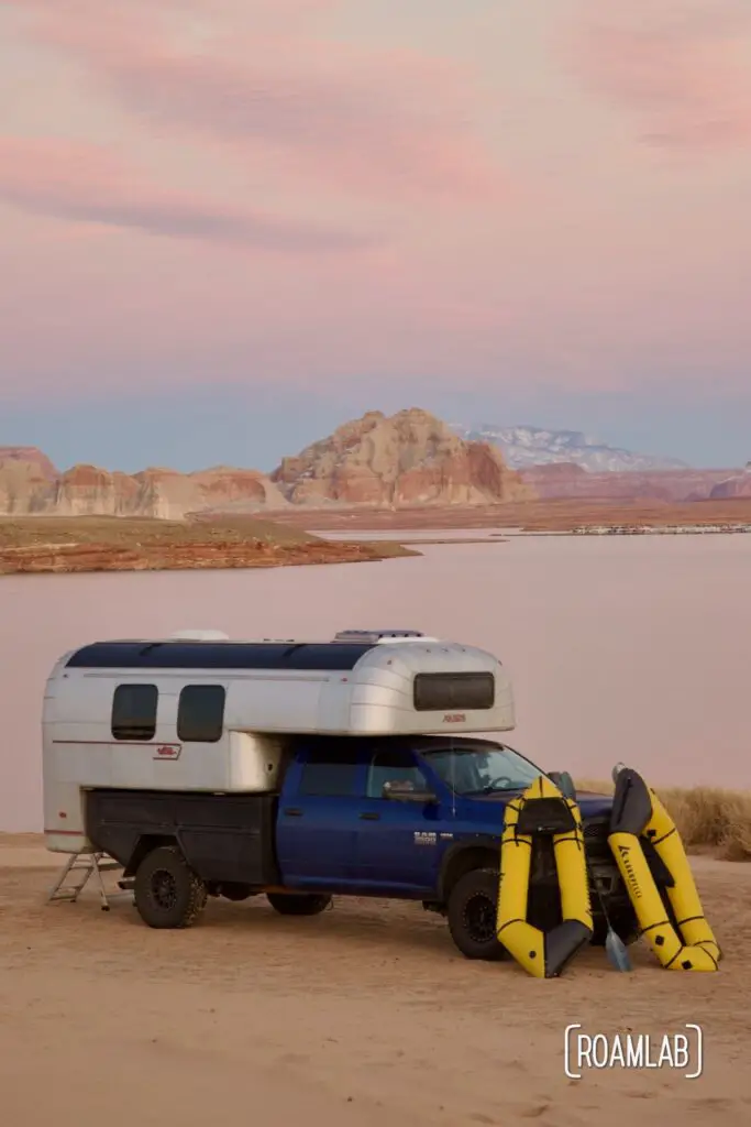Avion C11 truck camper parked on a sandy beach at sunset with pink buttes in the background and yellow rafts leaned up against the truck.
