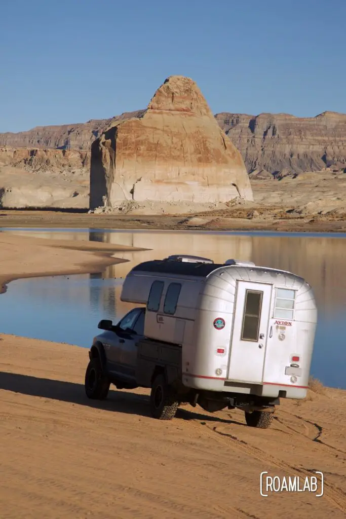 Avion C11 truck camper driving on a beach with Lone Rock towering in the background surrounded by Lake Powell.