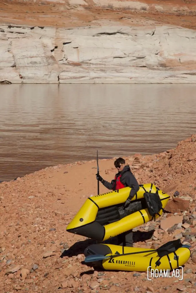 Man carrying a yellow inflated raft on a pink sand beach along Lake Powell in Northern, Arizona.