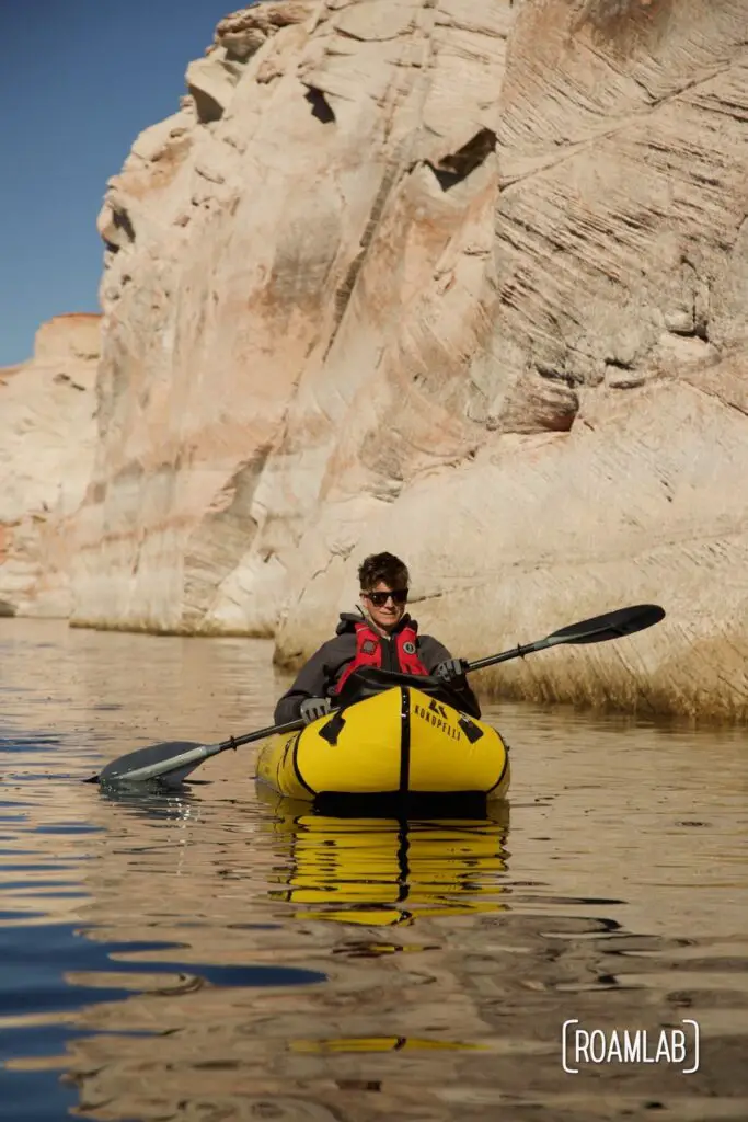 Man in a yellow raft paddling towards the camera with white cliffs dominating the background.