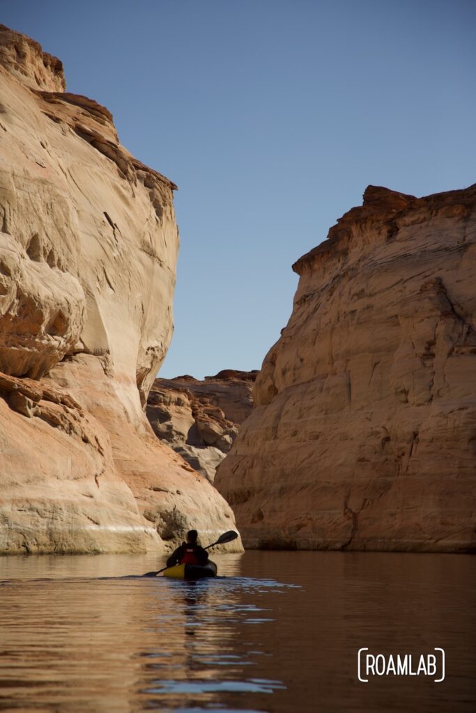 Silhouette of a man paddling in a raft towards golden cliffs that form the mouth of Antelope Canyon off Lake Powell in Northern Arizona.